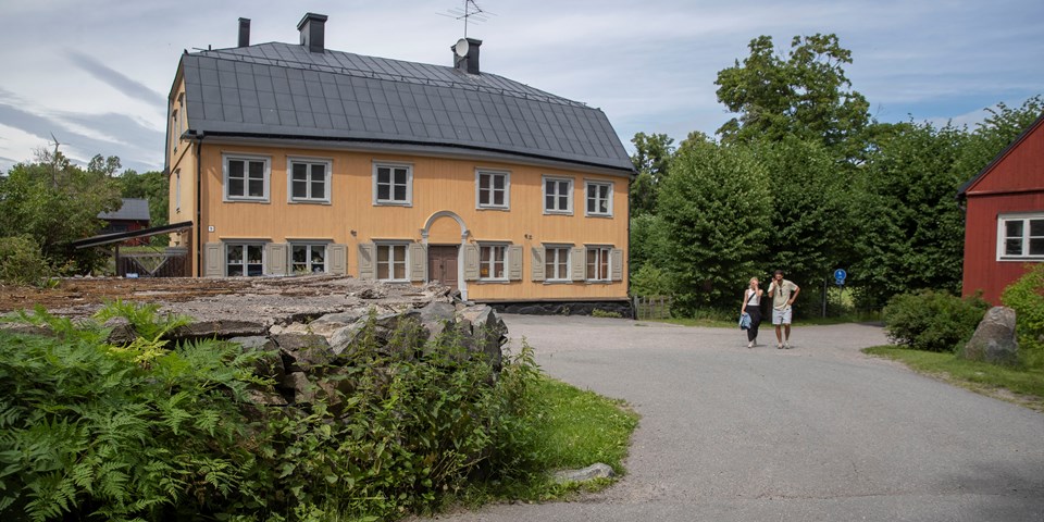 Två personer promenerar framför ett gult hus.