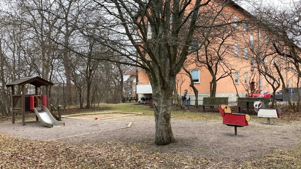 En lekplats med sandlåda, ett lågt lekhus med rutschbana och gungdjur. 