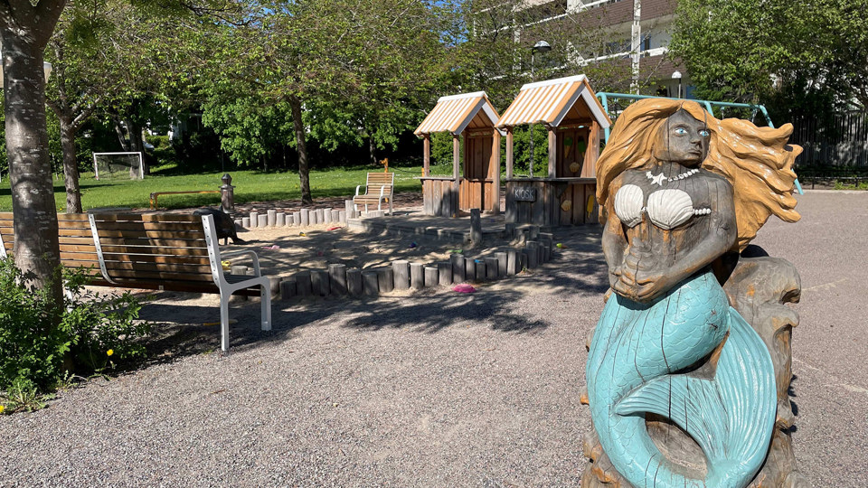 Sandlåda, lekhus, sittplatser och en träskulptur som föreställer en sjöjungfru.