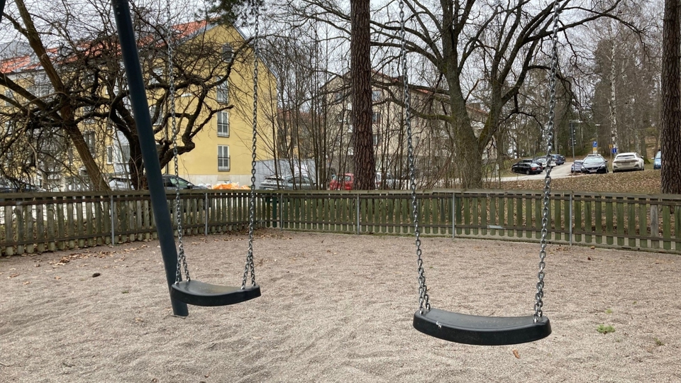 Två gungor på en lekplats bland flerfamiljshus.