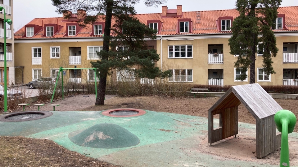 Lekyta med litet trähus, en konstruerad liten kulle och sandlåda, i bakgrunden flerfamiljshus, foto
