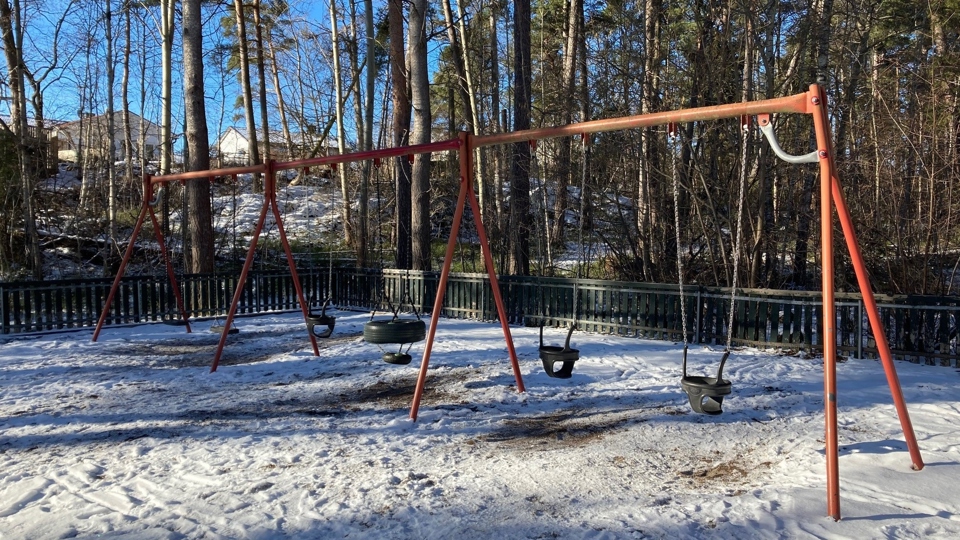 Lekplats med gungor samt träd och flerfamiljshus i bakgrunden