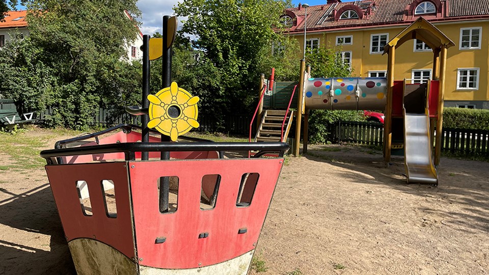 Lekplats med klätterställning i rött och gult, rutschkana och en båt.