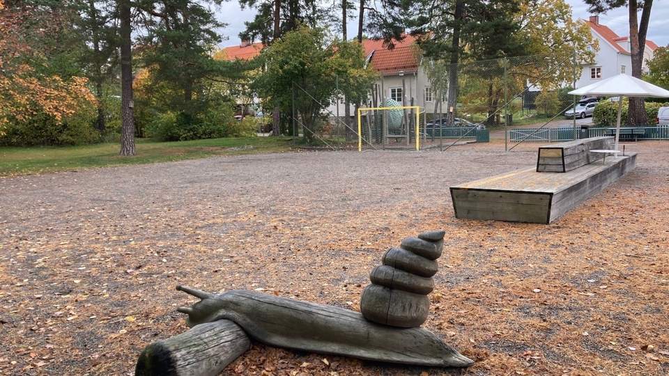 En grusplan med fotbollsmål. Bredvid planen finns bänkar och en lekskulptur.
