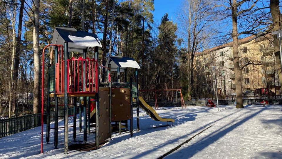 Lekplats med klätterställning och rutschkana samt träd i bakgrunden