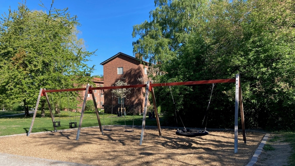 Gungställning med stora träd och ett flerfamiljhus i bakgrunden