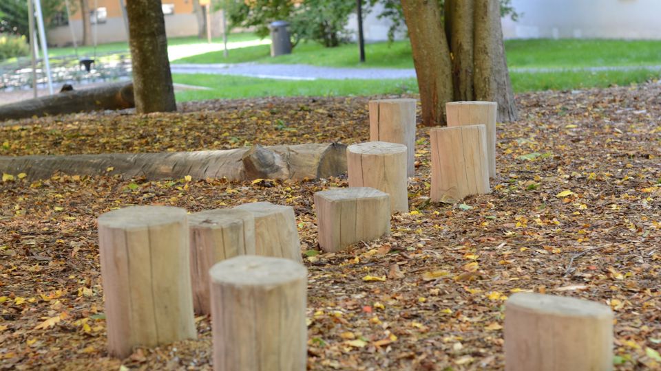 Lekplats med balanslek, grönska och flerfamiljshus i bakgrunden