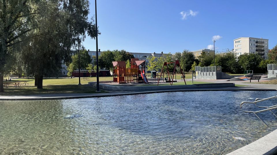 Plaskdamm med lekpark, träd och hus i bakgrunden.