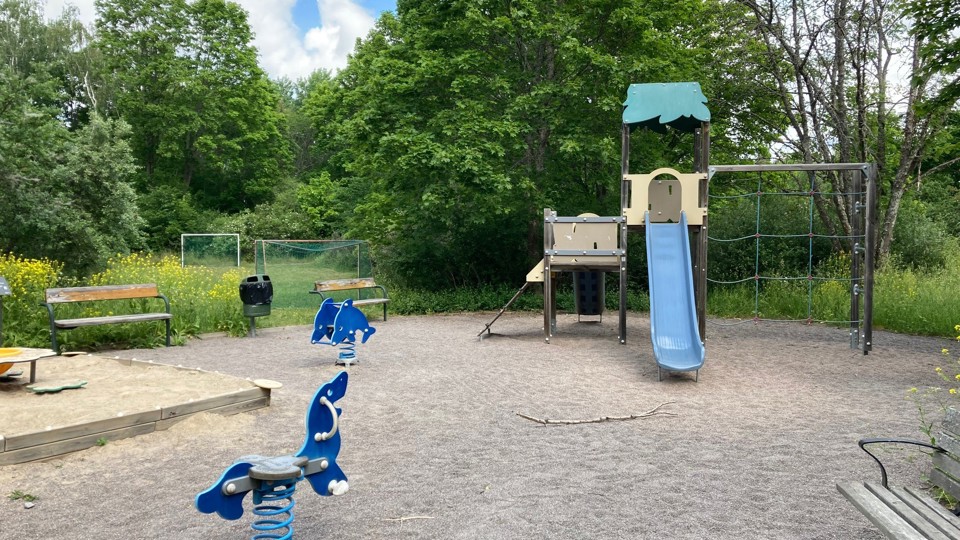 En lekplats med ett lektorn med rutschbana, sandlåda, bänkar och gungdjur.