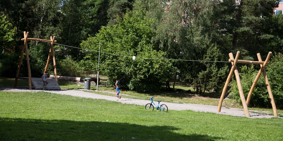 Barn leker med en linbana i en park omgivna av grönt gräs och grönskande träd.