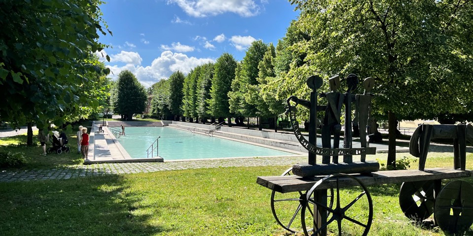 Konstverk och spegelbassäng i lummig park.