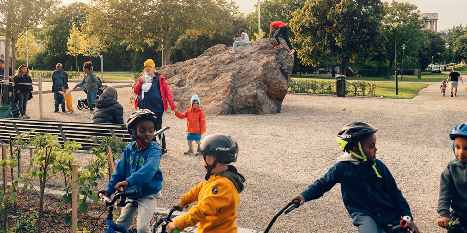 Barn klättrar på ett stort stenblock som finns mitt i parken. I bakgrunden kan man skymta ett vattentorn.