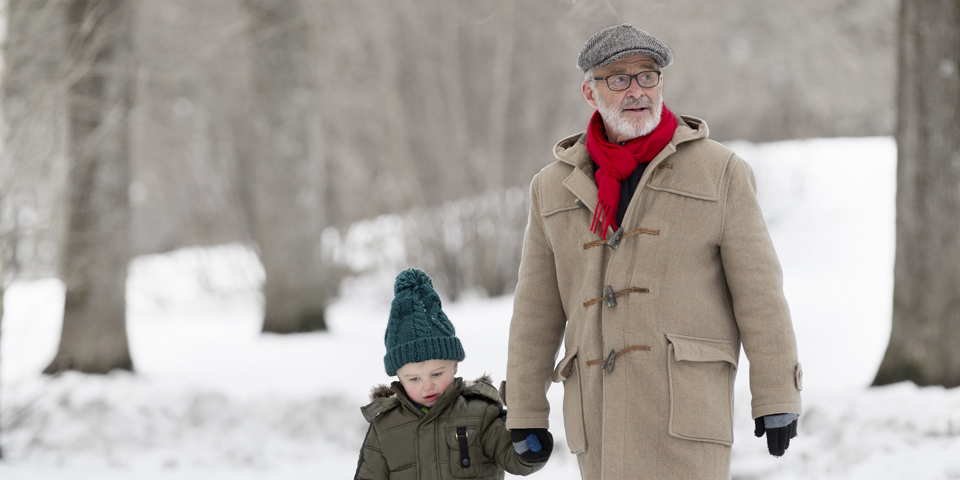 Barn och äldre man som går i en vinterklädd trädallé. Foto.