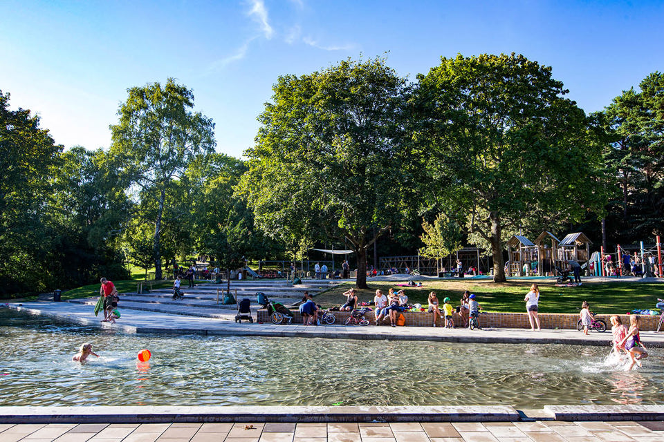 En grönskande park med en stor plaskdamm med stenläggning runt.