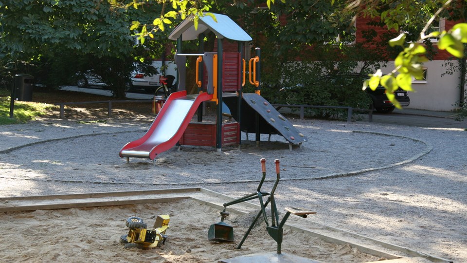 Rutschkana och sandlåda i en lummig kvarterspark.