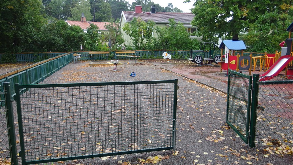 Lekplatsen med fjädergungor och multilekställning, inhägnad av staket.