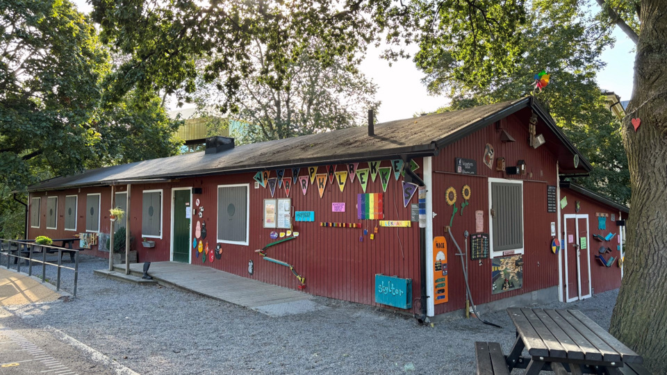 Parklekens röda trähus, inbäddat bland träd. 