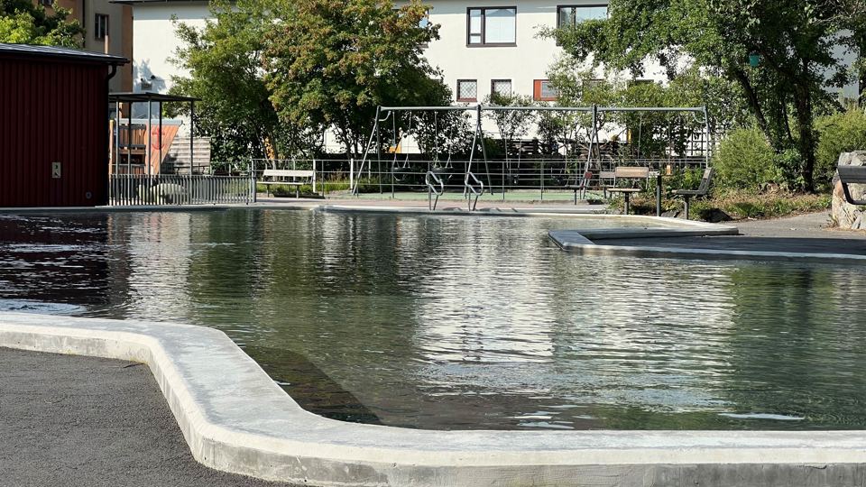 Plaskdamm med liten lekplats och bostadshus i bakgrunden.