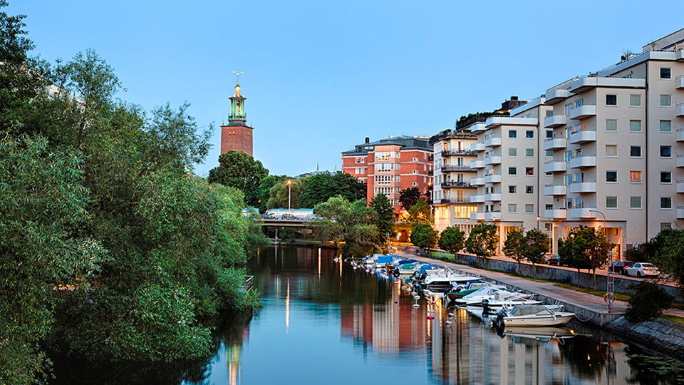 Båtar uppradade bredvid varandra i Karlbergskanalen. I bakgrunden skymtar en bro, flera bostadshus och Stadshuset.