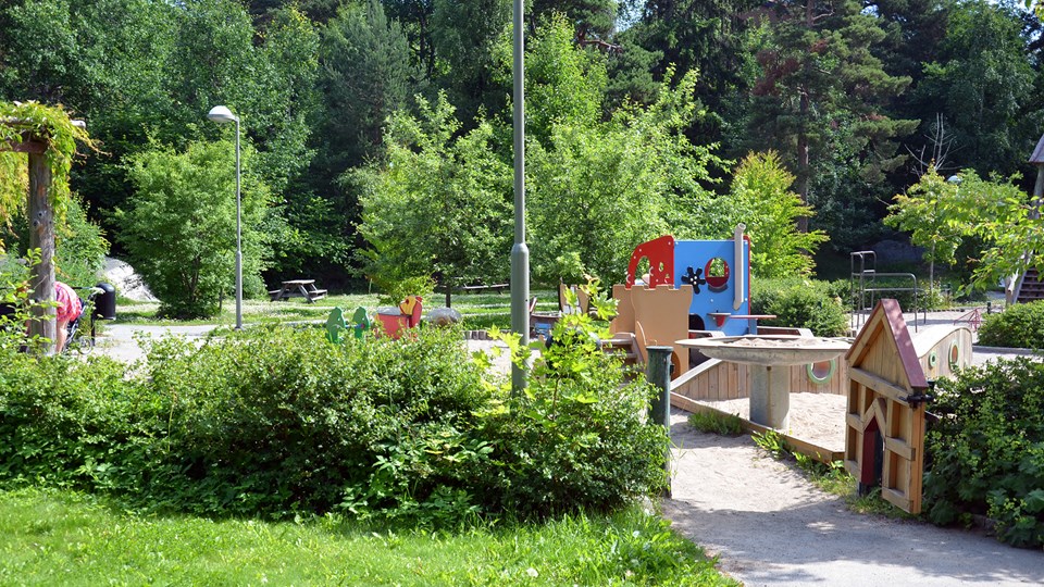 Lekparken omgärdad av gröna buskar och gräsmattor.