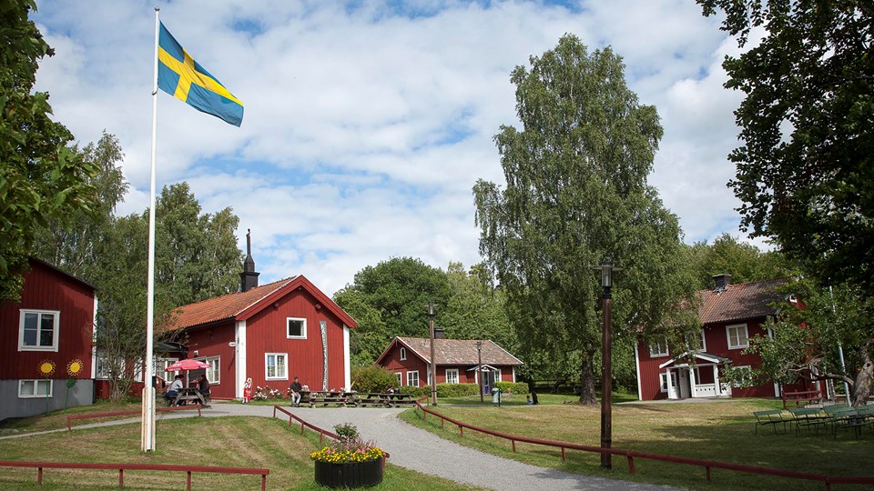 Rödmålade gårdshus i lummig grönska och med svenska flaggan i topp