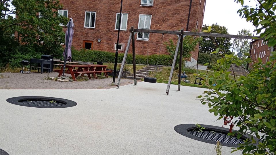 Lekplats med gungor framför ett bostadshus.